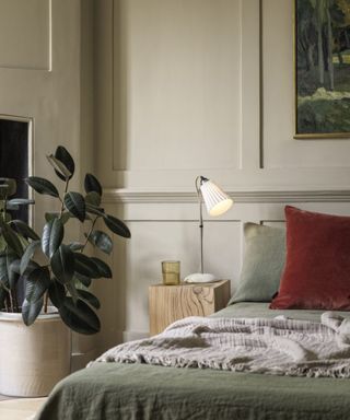 calming bedroom with houseplant, beige walls, green bedding and muted red cushion