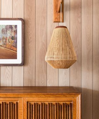 Wood panelled wall with wooden cabinet and rattan lampshade
