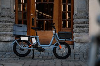 Blue Cake Åik cargo bike parked on cobbles, with front and rear carriers