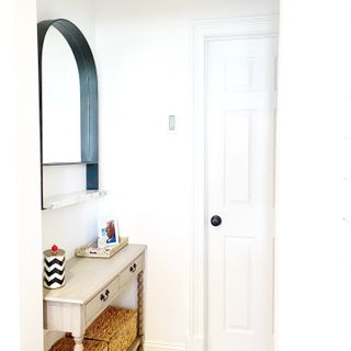 A white entryway from a side angle with mirror, console table and decorative ornaments.