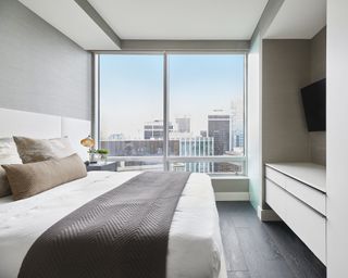 A bedroom TV idea with a television in the alcove between wardrobes, in a modern apartment bedroom with city views