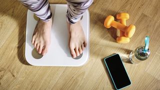 Woman's feet on smartscales, next to some light dumbbells and a phone