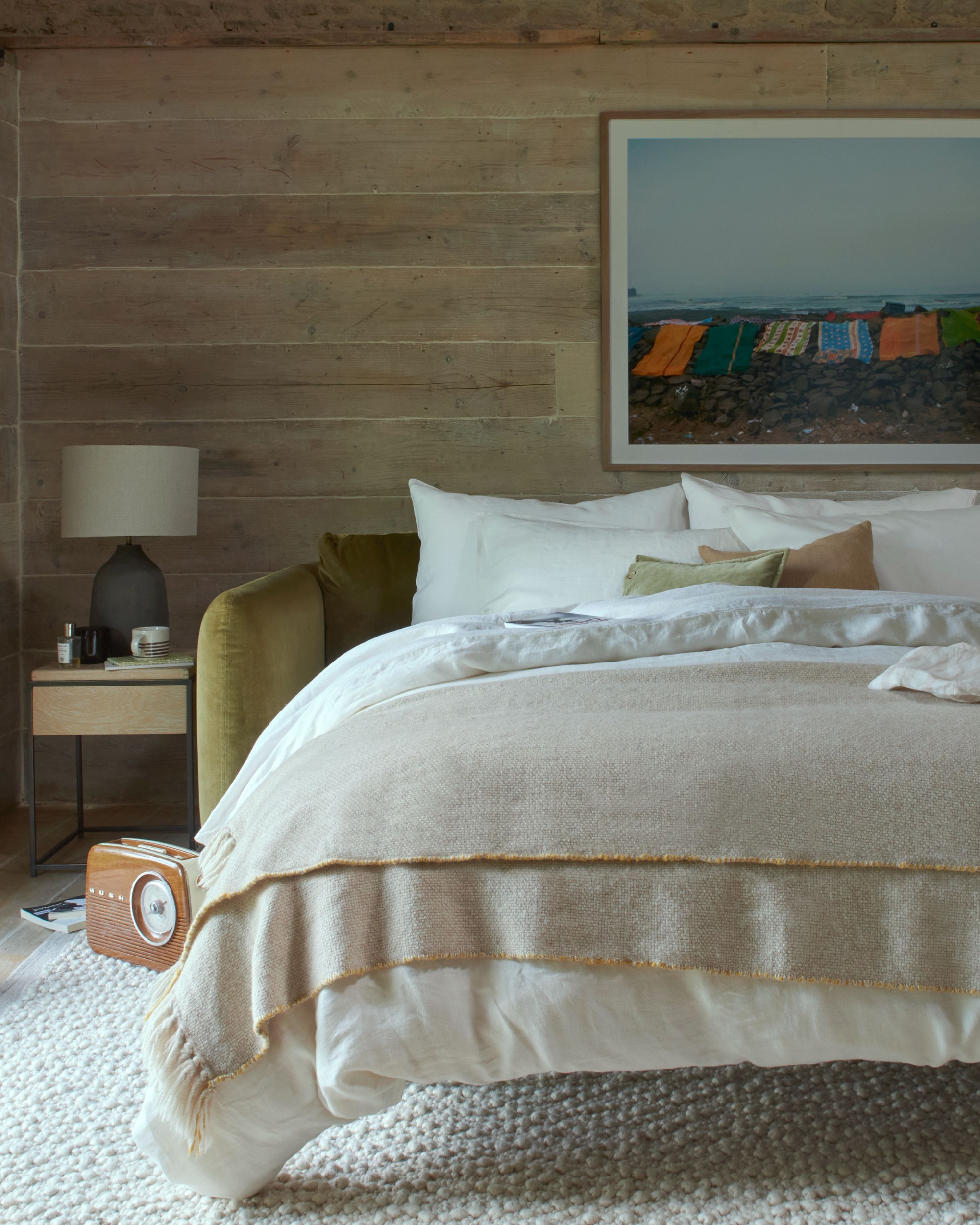 Image of a pulled-out and made sofa bed in a wood paneled room with an artwork of the beach over the bed and a textured, off white rug underneath.