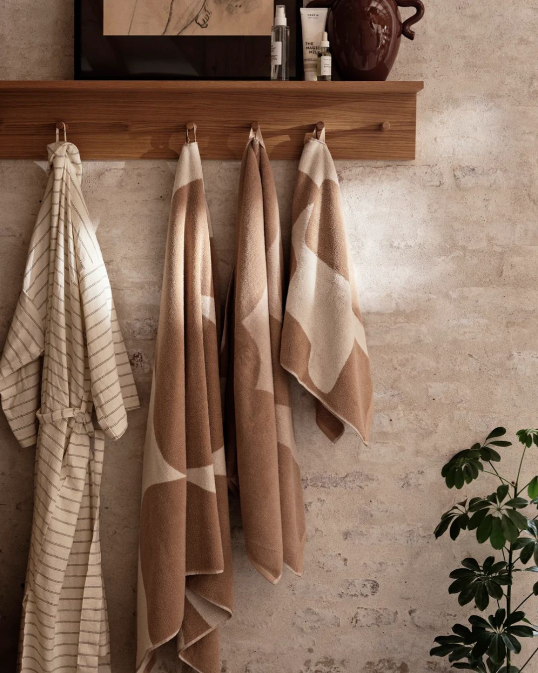 Ebb Beach Towel in Sand/Off-White hung up on a wooden rail against a bare cement and brick wall.