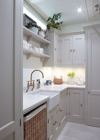 Fitted pale gray cabinetry in an L-shaped small laundry room, with white countertop and floor tiles.