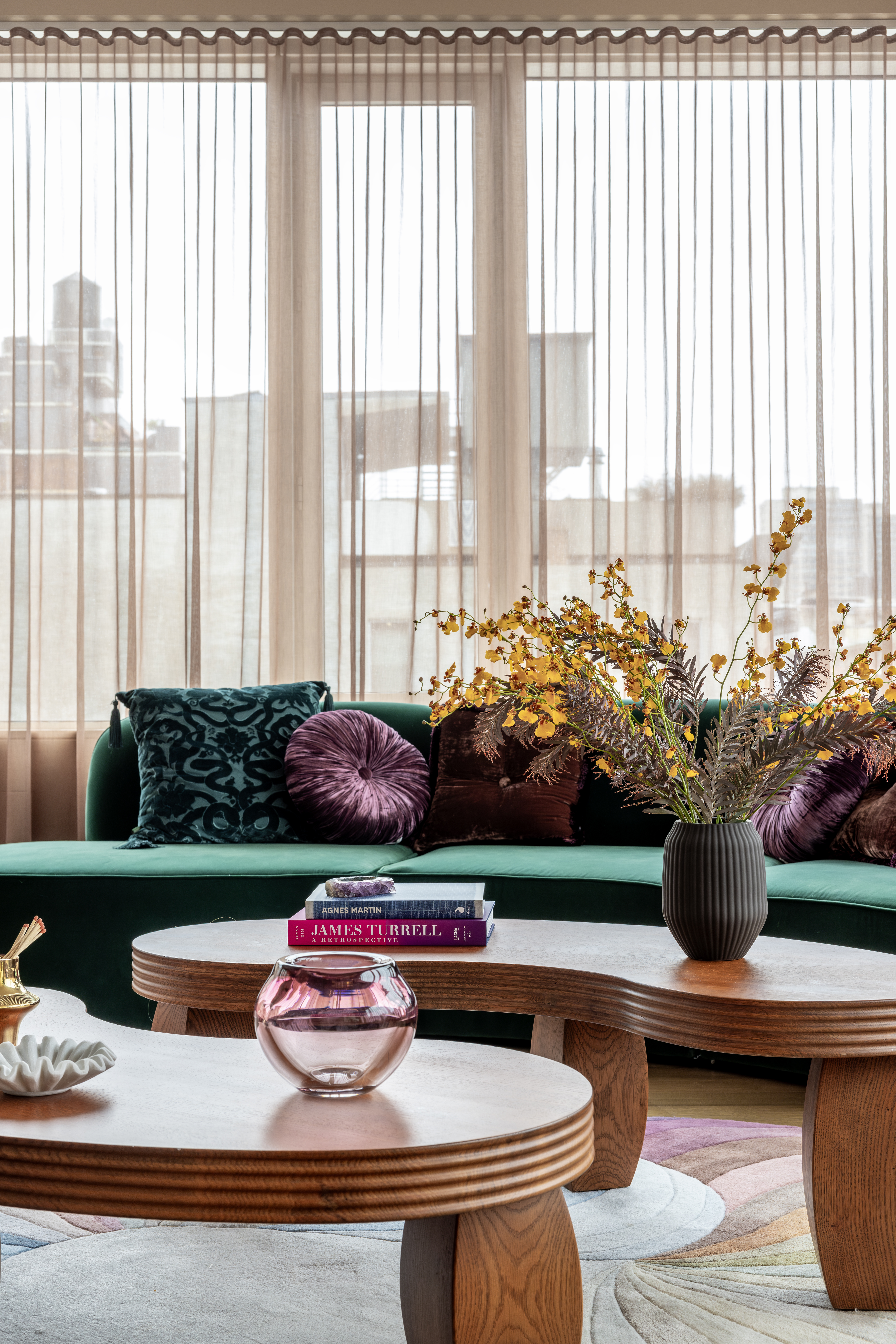 A living room with deep green, curving sofa, and soft pink curtains