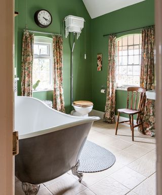 Green painted bathroom with floral curtains and free-standing grey painted bathtub