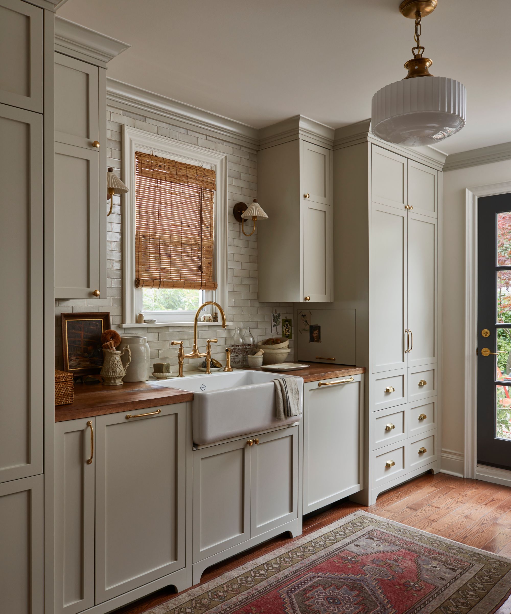 A galley kitchen decorated in a vintage style with gray cabinets, wood counters, and a vintage style rug