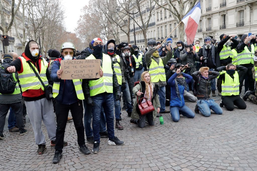 A protestor holds a sign reading &amp;#039;Macron stop hiding&amp;#039; near the Champs Elysees avenue in Paris on December 8, 2018 during a &amp;#039;yellow vests&amp;#039; protest.