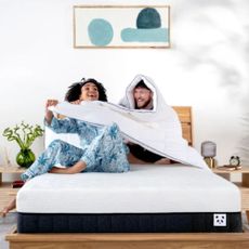 Woman and man on Panda London mattress, laughing. Man with duvet over his head, which woman is pulling.