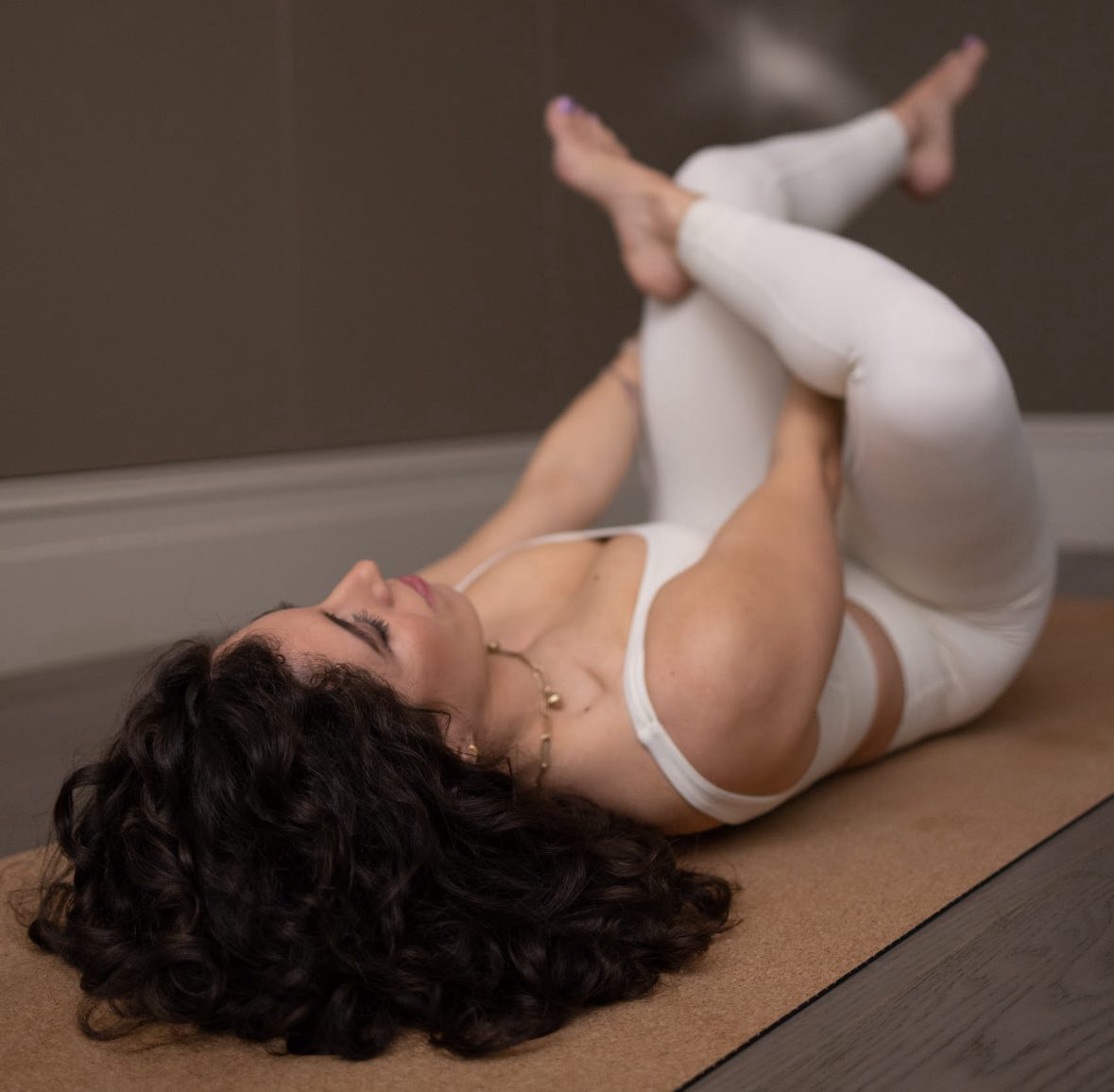 Rebecca Daodun stretches on a Pilates mat. She is lying down, with her right ankle crossed over her left knee, pulling her left thigh towards her torso.