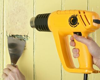 Using a heat gun and scraper to strip paint from a wooden surface