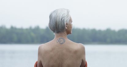 Woman looking out over water with a tattoo visible on her neck