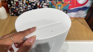 A finger operating the volume trough slider control on top of a white Sonos Move 2 speaker.