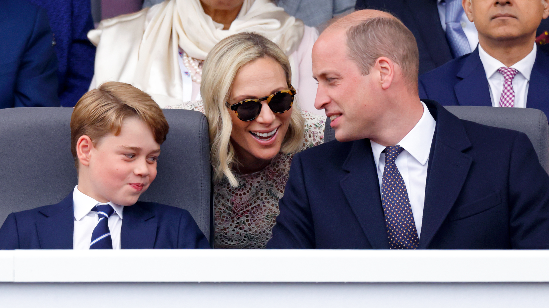 Prince George smirking as Zara Tindall leans over and talks to Prince William