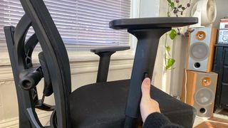 A hand adjusting the armrest on an office chair