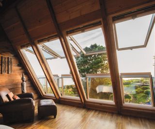 large wooden timber rooflights in timber clad loft conversion with leather armchair in front of windows