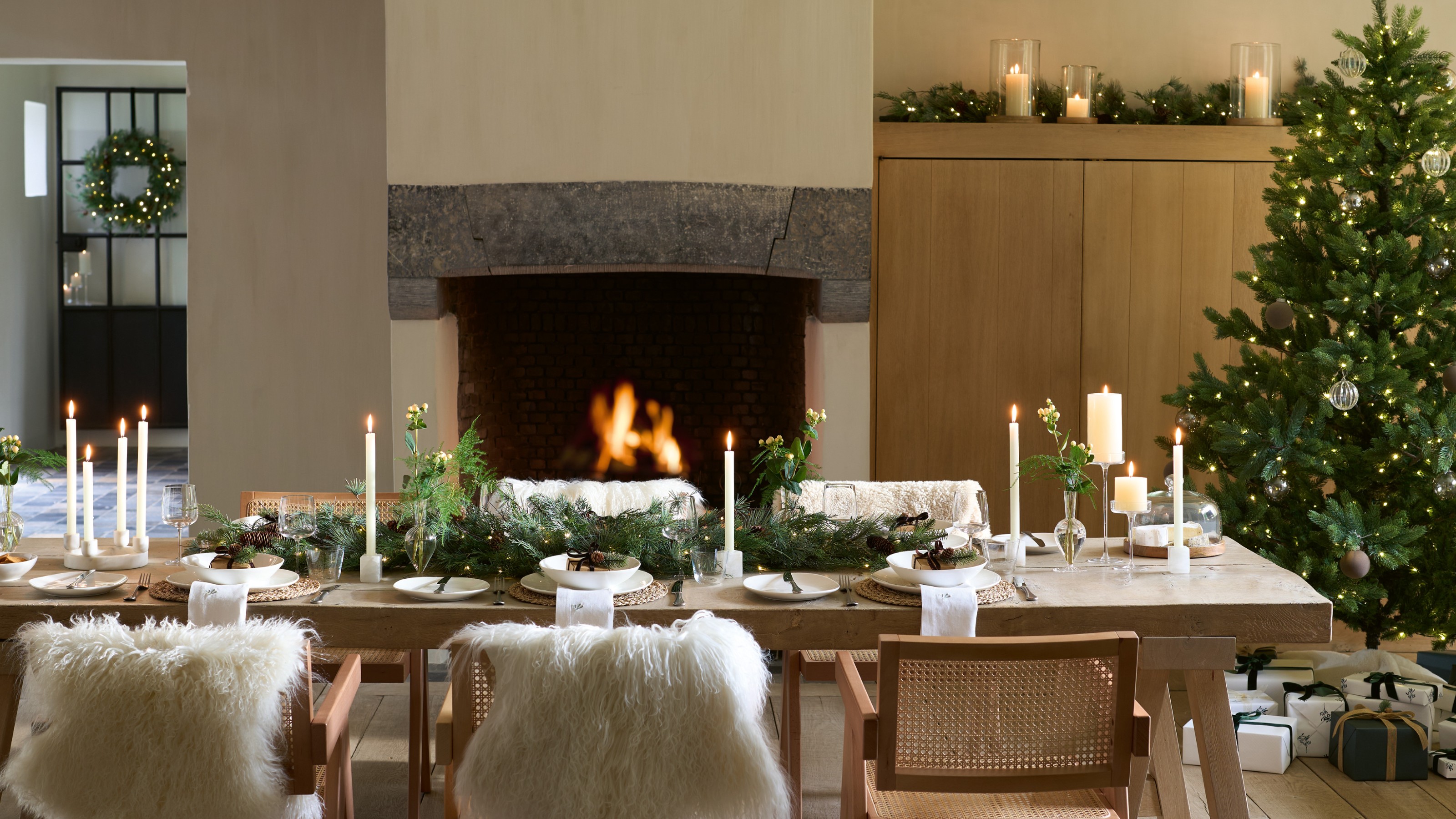 A large dining room with a long rectangular dining table decorated with The White Company&#039;s garland and tree in the corner