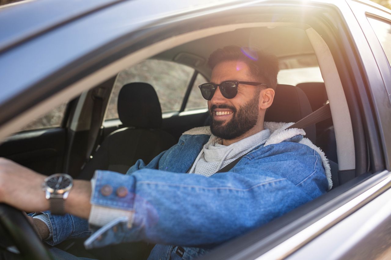 A handsome, happy man in sunglasses in the front seat of a car