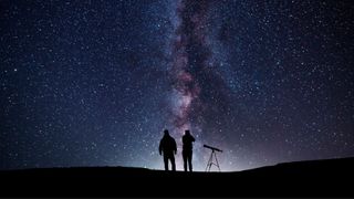 Two people with telescope looking up at starry sky