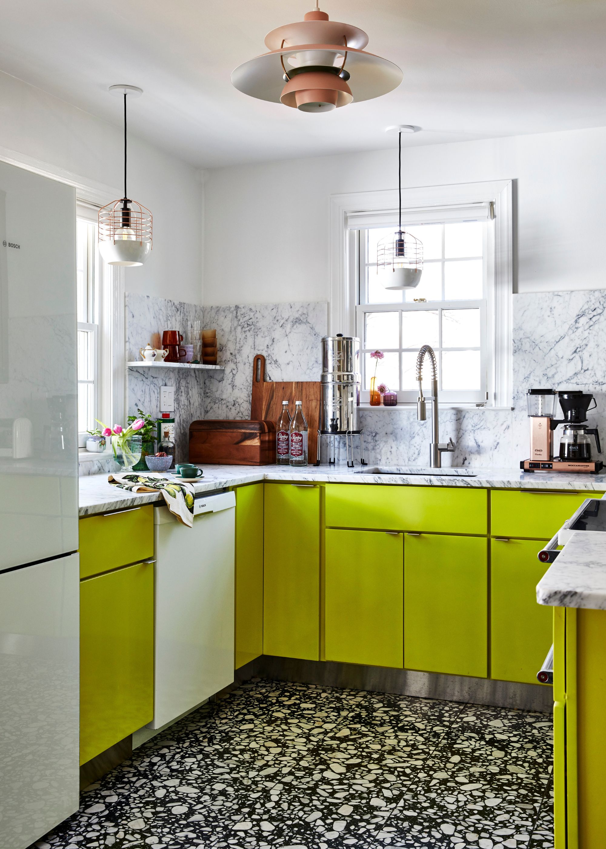 A modern kitchen with bright chartreuse lower cabinets, white walls, marble counters and backsplash, and black and white terrazzo floors.