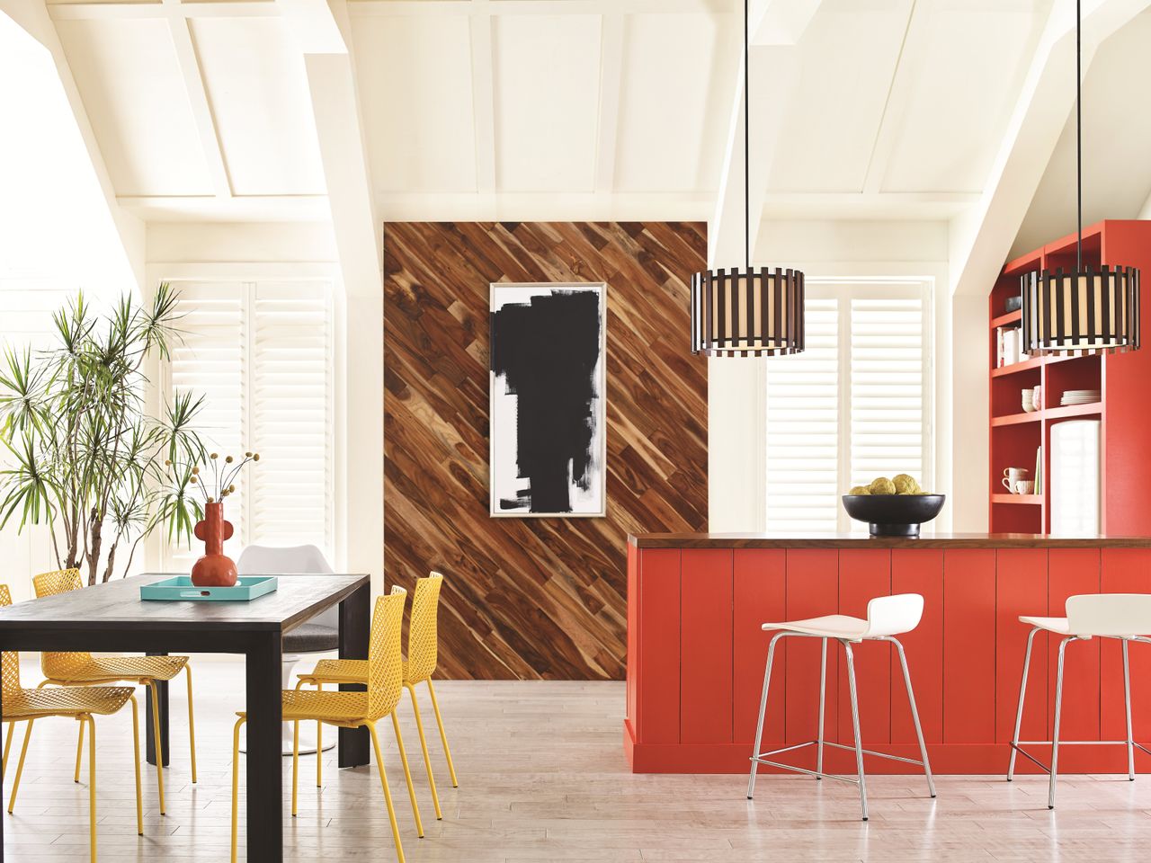 A bright modern kitchen with red cabinets and a black dining table with yellow metal chairs