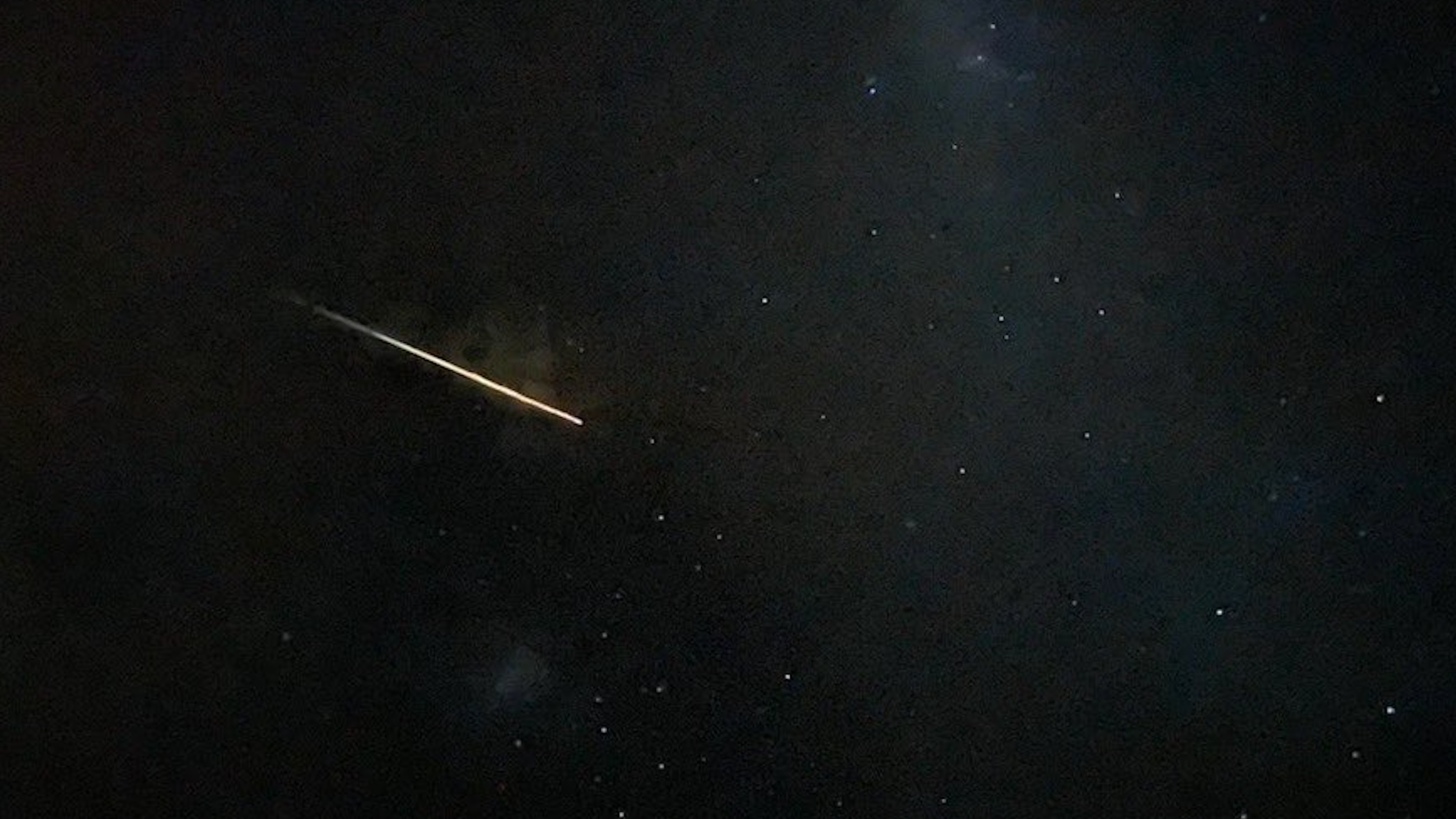 a yellowish fireball streaks through a dark night sky