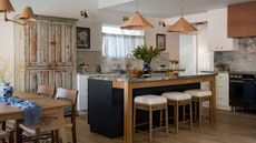modern chefs kitchen with white cabinetry, a terracotta plaster hood and navy kitchen island with blue marbled countertops with vintage accessories