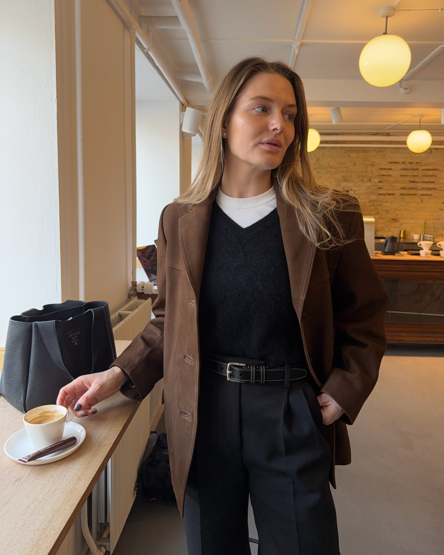 Woman wears brown blazer, white T-shirt, black v-neck jumper, black tailored trousers and black belt.
