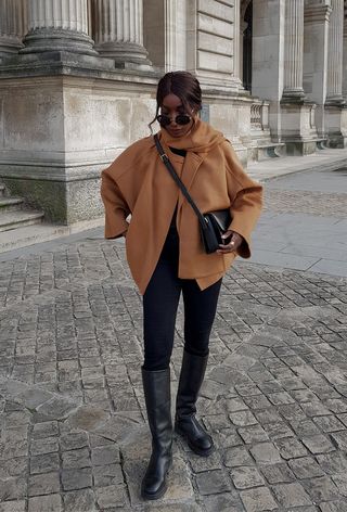 best riding boots shown in a photo of a woman in Paris wearing a tan scarf coat with black skinny jeans and black riding boots