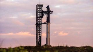 a silver rocket stands upright at sunrise in front of pink and orange clouds