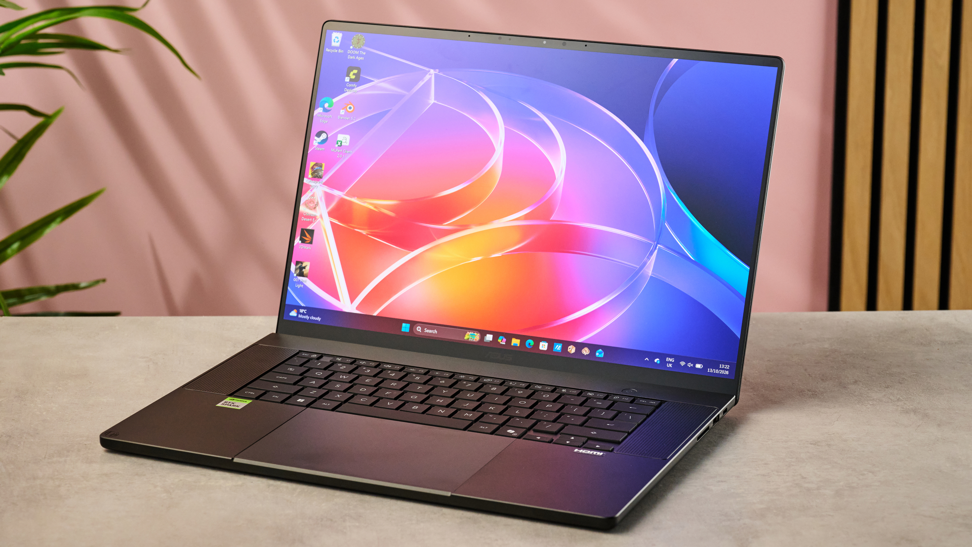 The Asus ProArt P16 RTX Spark next to a potted plant, in front of a pink wall with some wood cladding.