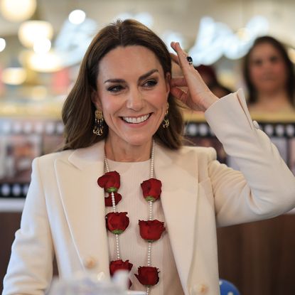 Princess Kate wearing a white coat and red rose garland smiling