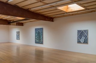 A gallery room with exposed steel girders, wooden floor, and three pieces of artwork