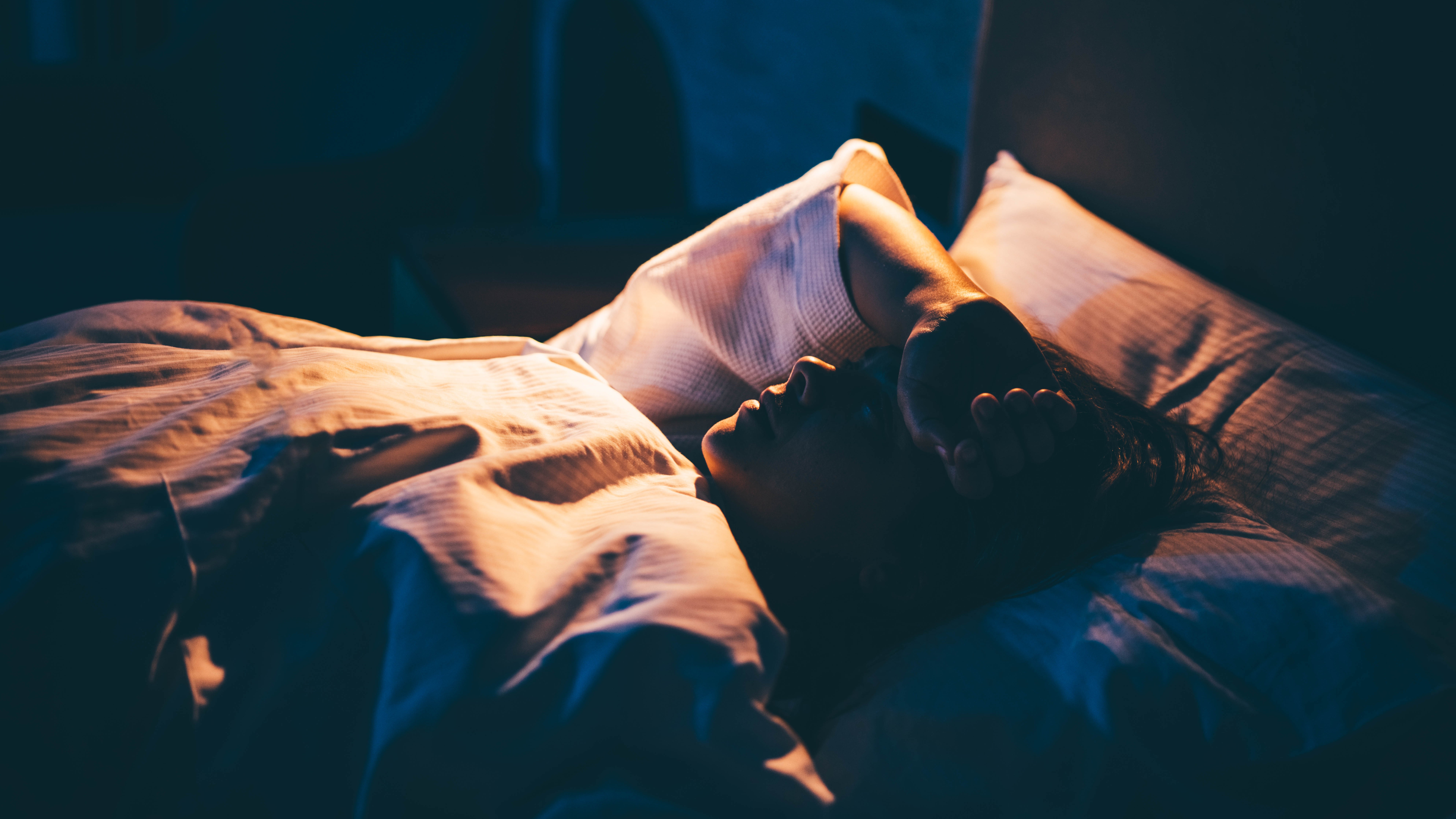 photo of woman lying in bed with an arm resting on her forehead