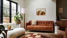 We've created your checklist for moving into a first house. Here is a white living room with a tan couch with a brown wall art print above it, a tall white lamp, and a light and dark brown checked rug