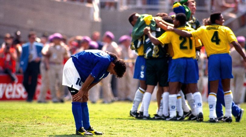 Italy forward Roberto Baggio stares at the ground in dejection after his missed penalty in the 1994 World Cup final as Brazil players celebrate the title.