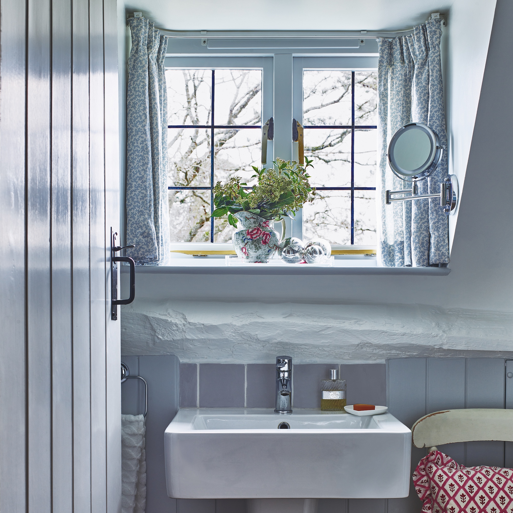 small grey painted bathroom with white basin and casement window with pale blue grey curtains