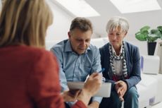 Mature Couple Meeting with Financial Advisor, selective focus to senior man and mature woman listening to financial advisor. She is pointing with pen to digital tablet and speaking about reti