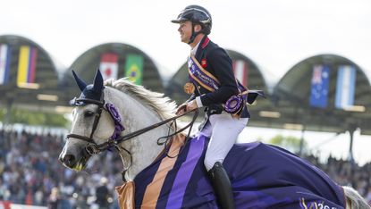 Harry Charles, a British rider, and LT Holst Freda, a grey horse, take a lap of honour after landing individual bronze at the showjumping World Championships, with the horse wearing a purple rug