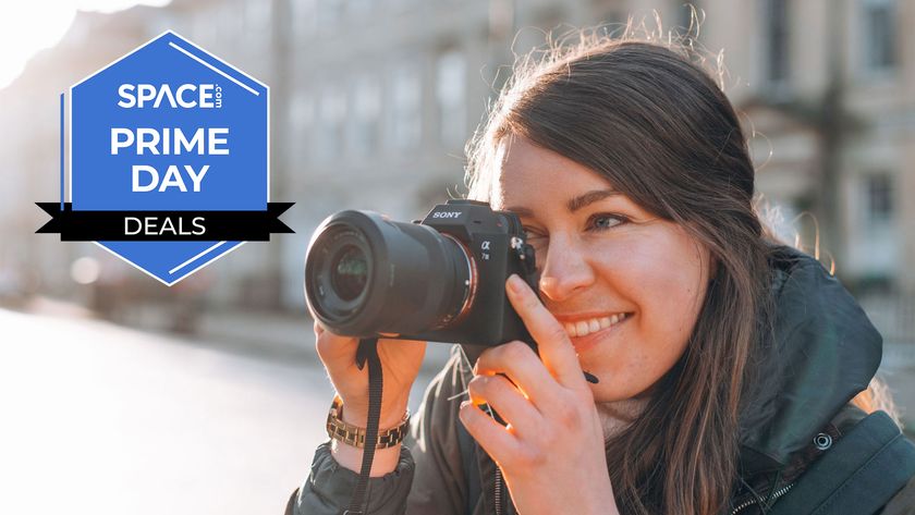A smiling woman looking through the viewfinder on a Sony A7 III with buildings in the background. 