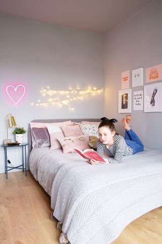 Light purple child's room with pink scatter cushions, art prints framed on the wall, and a neon heart sign