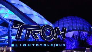 a sign reading "Tron Lightcycle Run" in front of a domed building lit up in blue