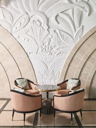 Bas relief mural with a small black table with four pink and black chairs in front of it.