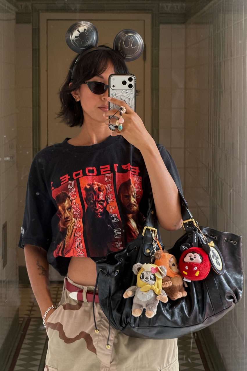 A woman wearing a black graphic Star Trek t-shirt with camo pants and a black bag with charms.
