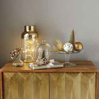 Mixed golds adding a festive accent for Christmas. Detail of glass ornaments and Christmas present on wooden cabinet
