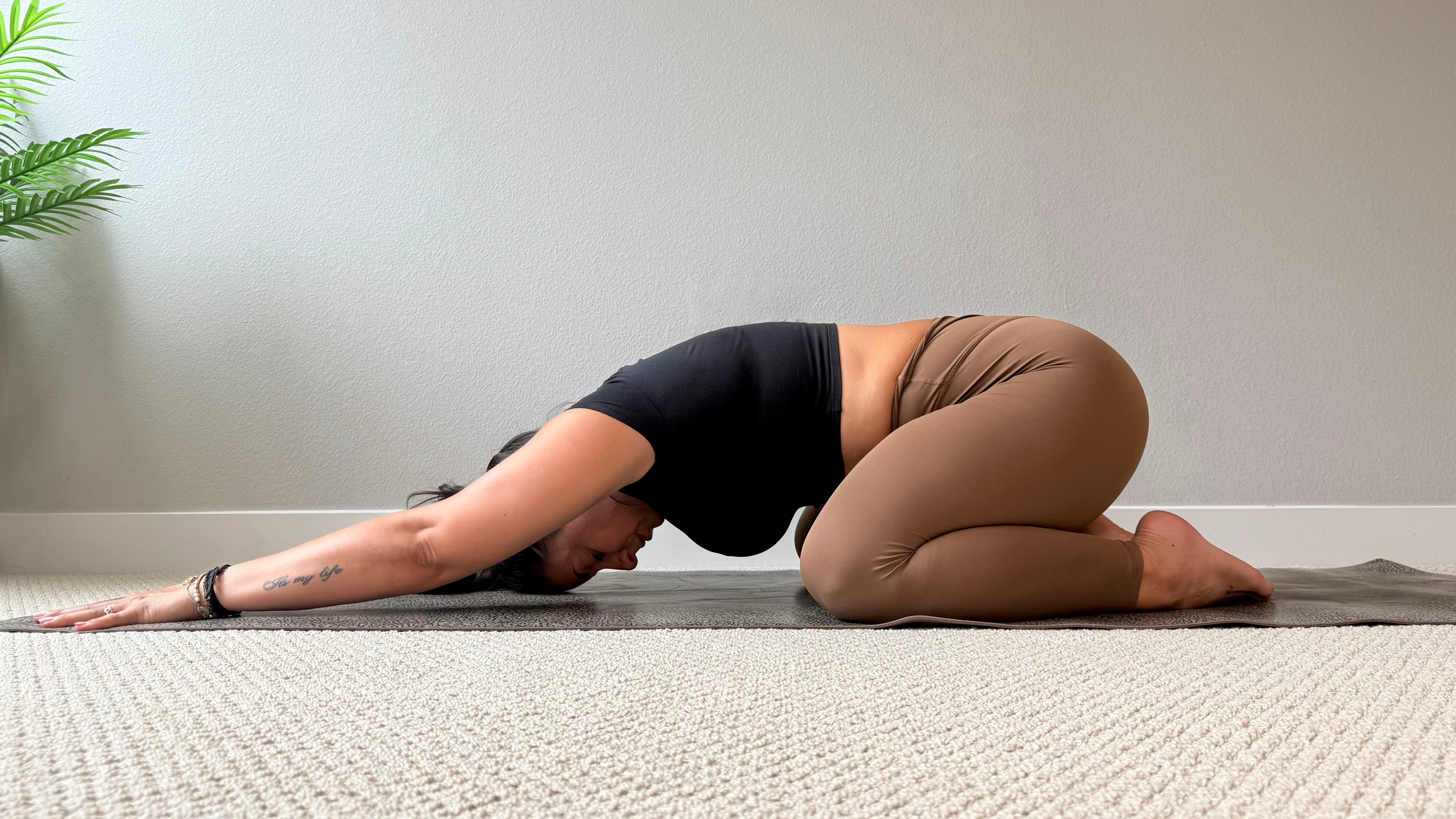Elma Panagaki performs child's pose on a yoga mat. Her knees are bent, chest close to the floor and arms extended on the floor above her head.