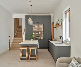 Contemporary kitchen layout with grey cabinets and light work surfaces and buff coloured stone floor