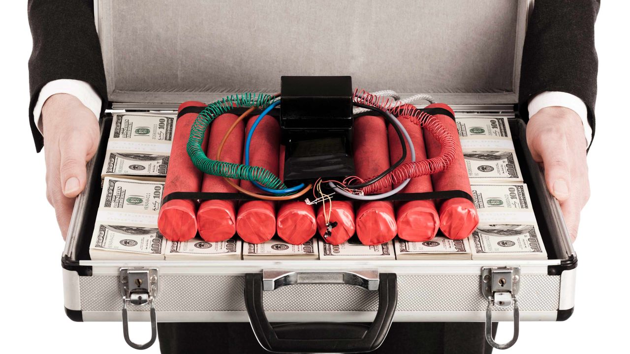 A bundle of dynamite sticks sits on top of a briefcase filled with stacks of money.