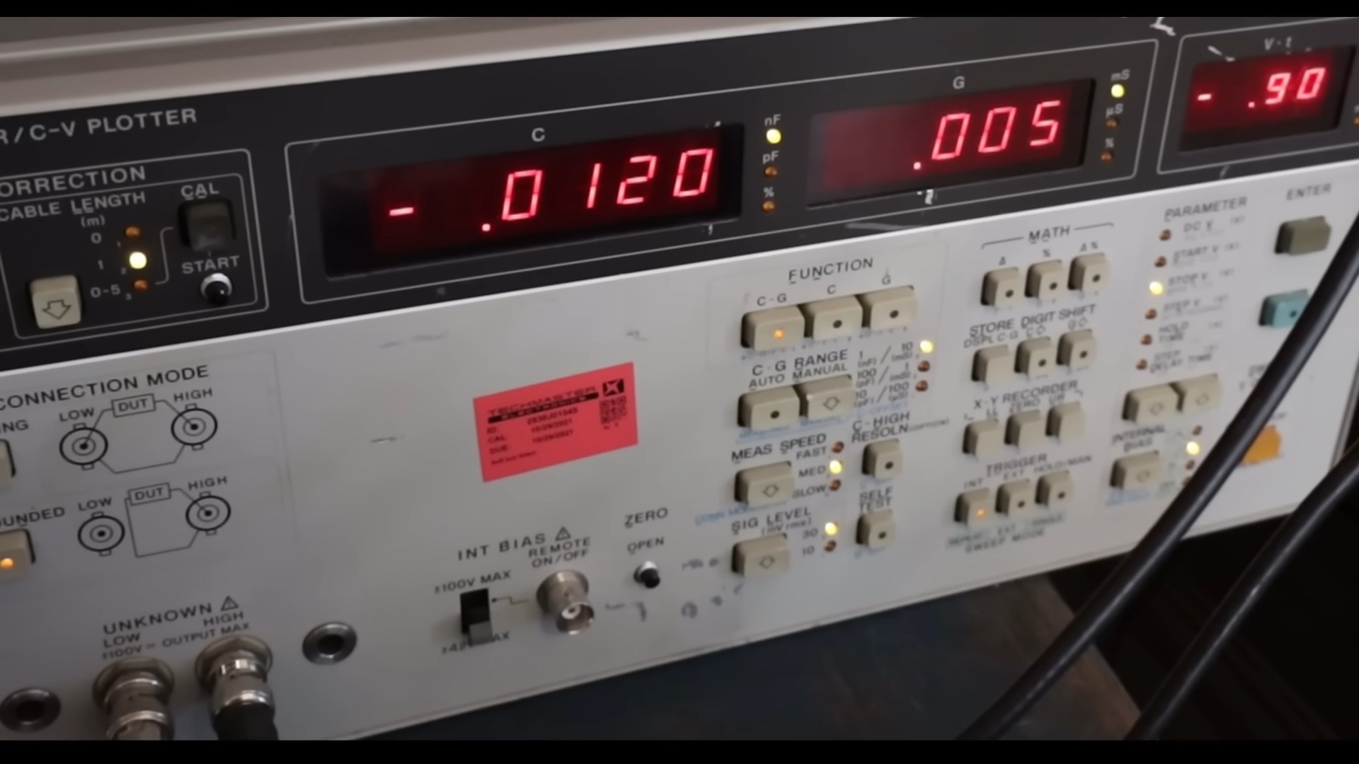 Close-up of an electronic testing device with digital readouts and numerous switches and buttons. Displays show numbers in red, indicating active settings.